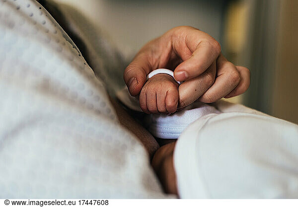 Mother's hand holding her newborn baby's hand while breastfeeding.