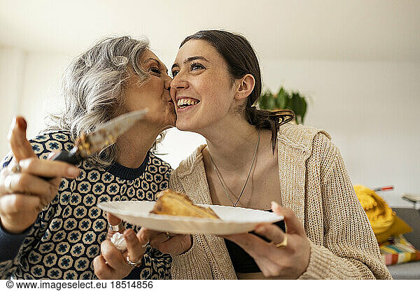 Mother serving cake and kissing daughter at home