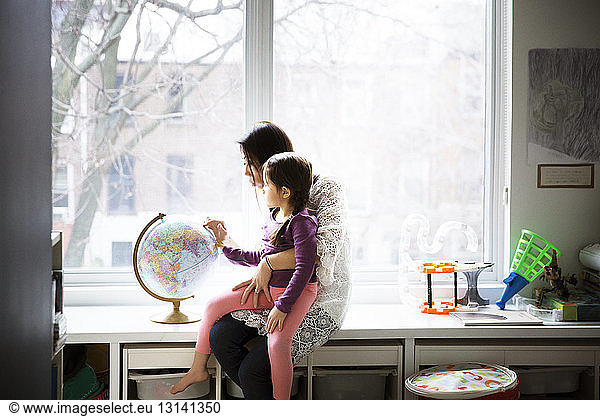 Mother showing globe to daughter against window at home