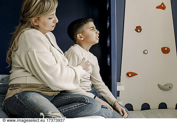 Mother sitting by autistic son in bedroom at home