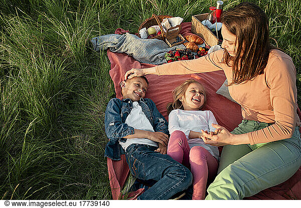 Mother sitting by happy children on picnic blanket