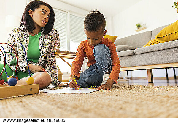 Mother sitting by son drawing at home