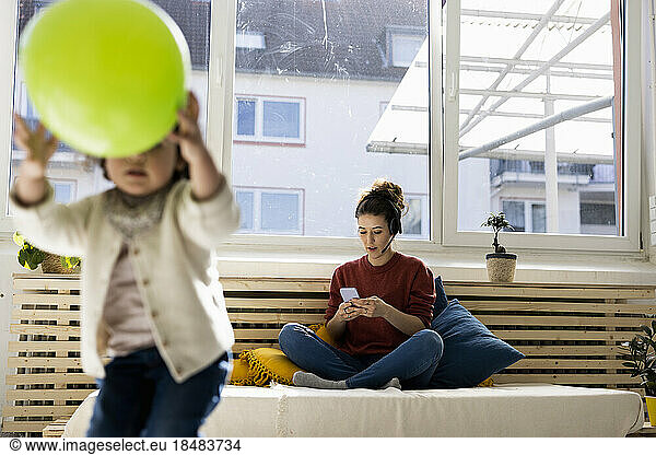 Mother sitting on couch talking over headset while daughter is plaing in foreground