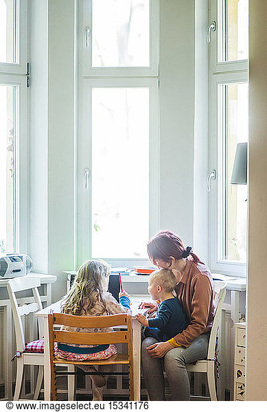 Mother sitting with son while assisting girl studying at table