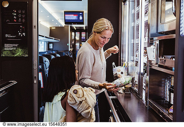 Mother standing with daughter while looking at food in train refrigerator