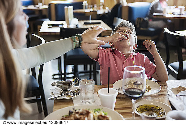Mother stopping son eating noodles in restaurant
