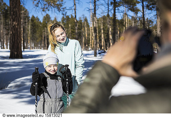 Mother taking a picture of her two children  a boy and teenage girl in snowy forest landscape.