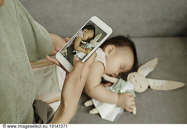 Mother taking picture of daughter sleeping at home
