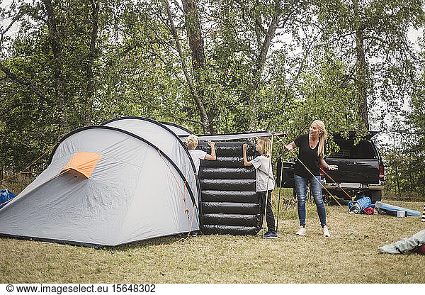 Mother talking to children carrying mattress in tent at camping site