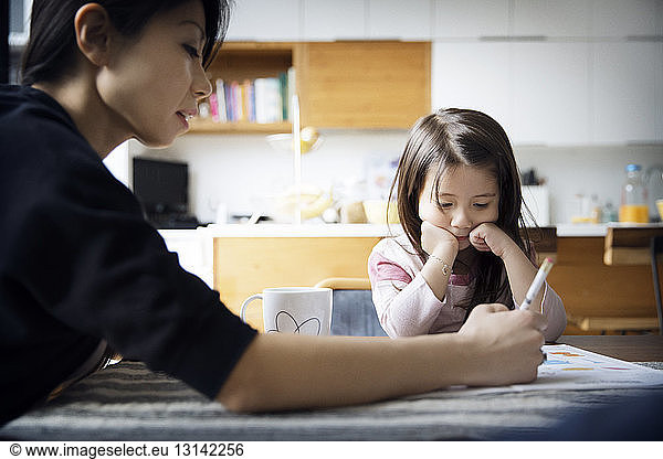 Mother teaching daughter on table at home