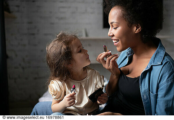 Mother teaching daughter to apply lipstick