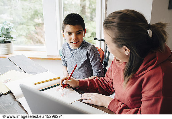 Mother teaching drawing to autistic son while sitting at home