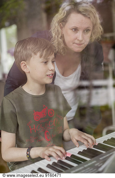 Mother teaching piano to son in house