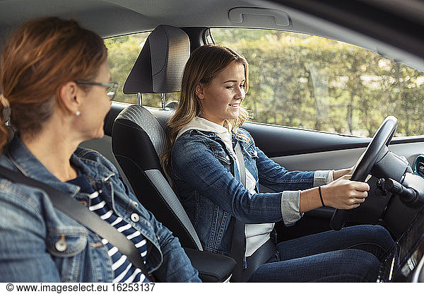Mother teaching smiling teenage girl driving during weekend