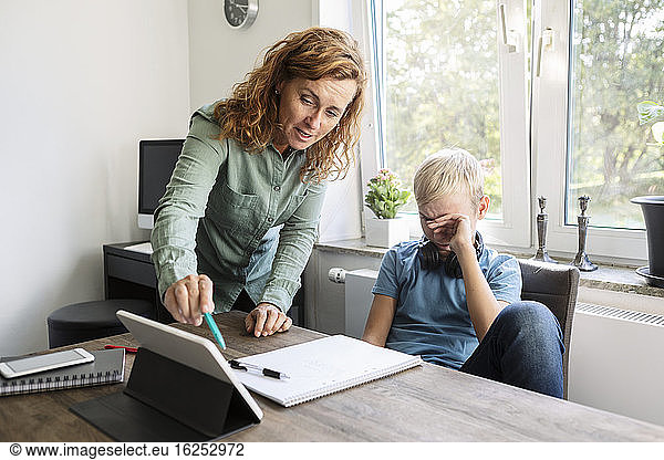 Mother teaching son on digital tablet at home