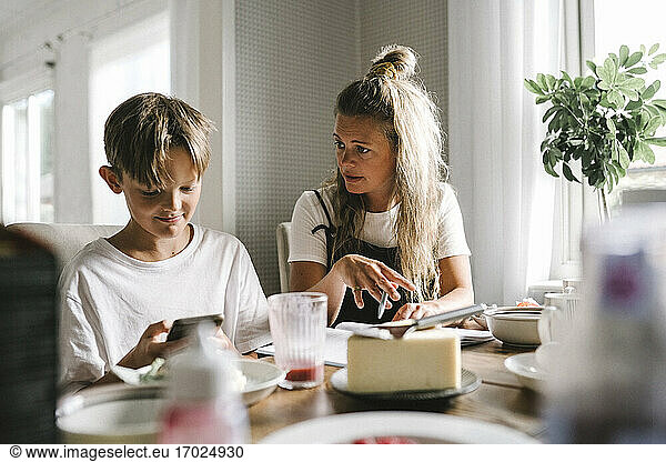 Mother teaching while son using smart phone at home