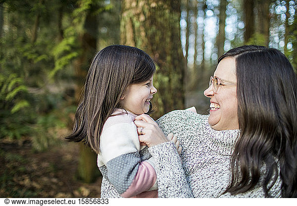 Mother tickling her daughter in outdoor setting.