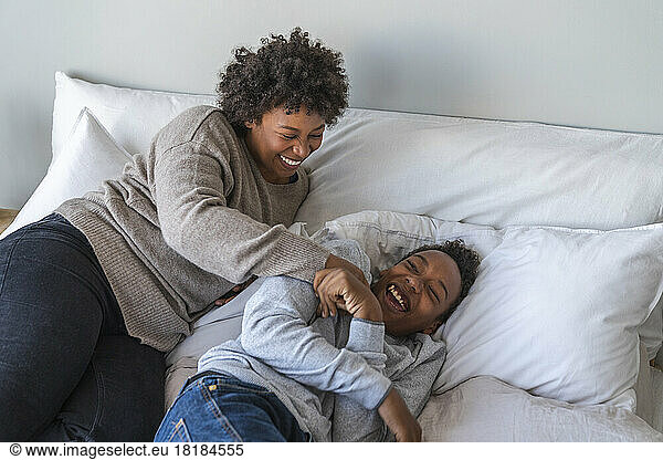 Mother tickling son lying on bed at home