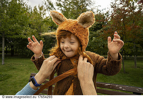 Mother tying bear costume hat of daughter at park