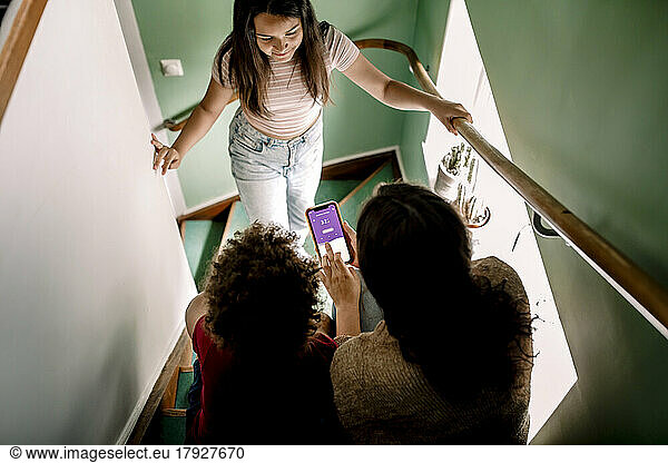 Mother using home automation app on smart phone with son and daughter at staircase