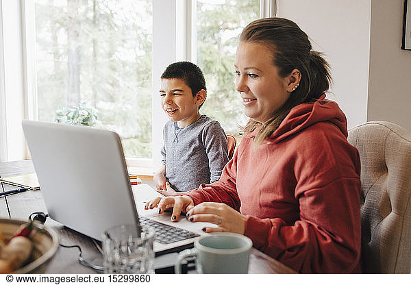 Mother using laptop on table while sitting with autistic son at home