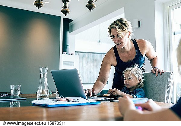 Mother using laptop while daughter sitting in living room at home