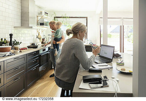 Mother using laptop while father cooking with son in kitchen