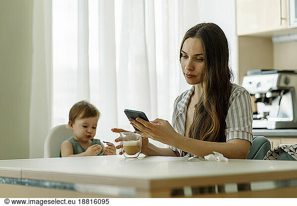 Mother using smart phone with daughter sitting on table at home