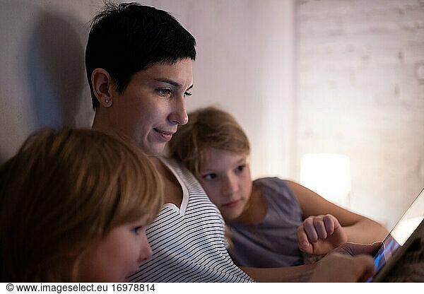 Mother using tablet near daughters on bed