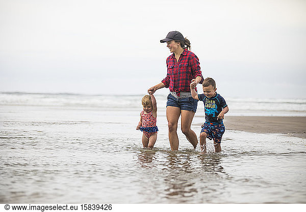 Mother wading into the ocean with her two children.