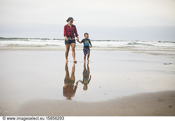 mother walking on beach  holding hands with her son.