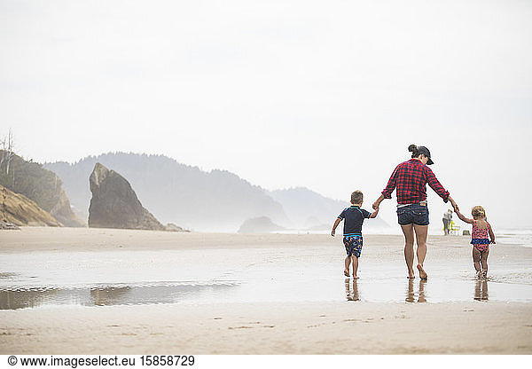 mother walking on beach with her two young children.