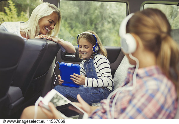Mother watching daughters with headphones using digital tablets in back seat of car