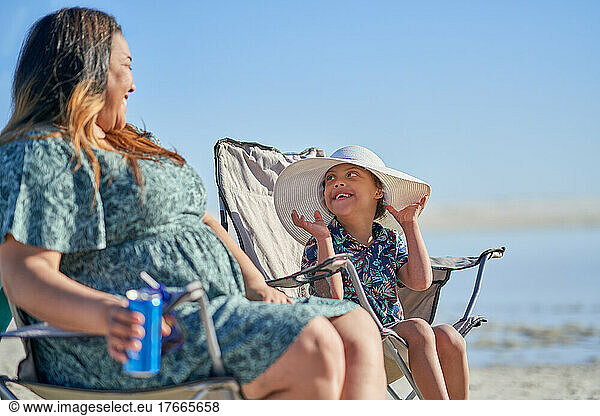 Mother watching happy cute son with Down Syndrome in hat on beach