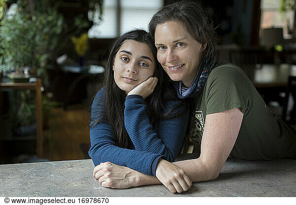 Mother with arms around pretty teen daughter looking at camera