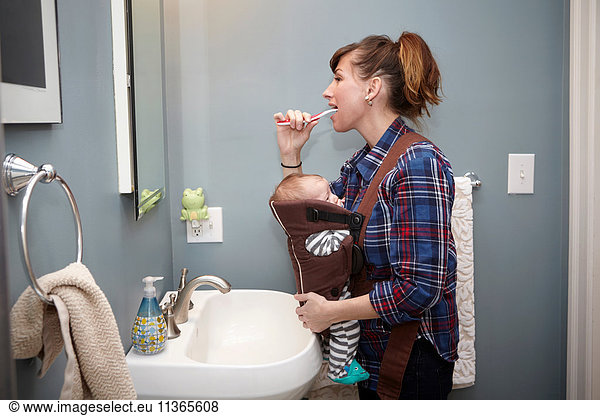 Mother with baby boy in baby sling  brushing teeth