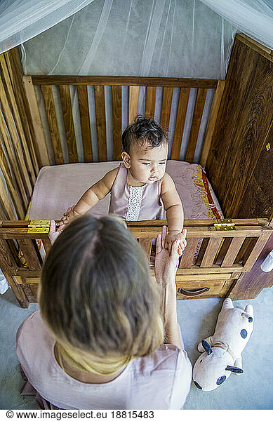 Mother with baby daughter playing in crib at home