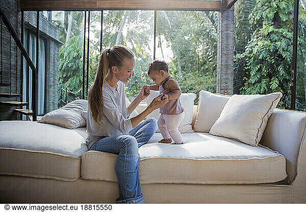 Mother with baby daughter standing on sofa at home