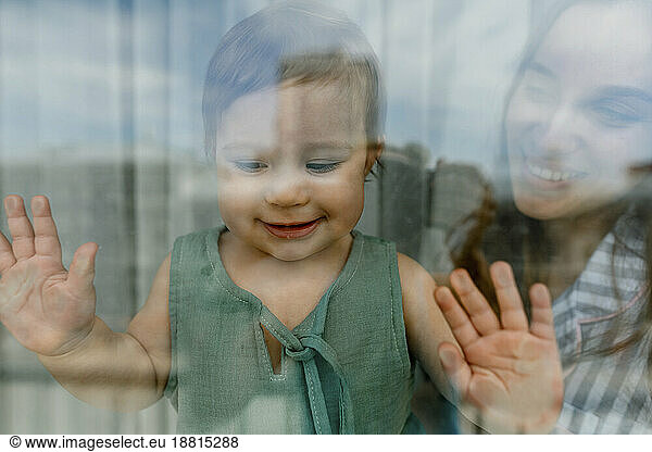 Mother with baby girl looking out of glass window