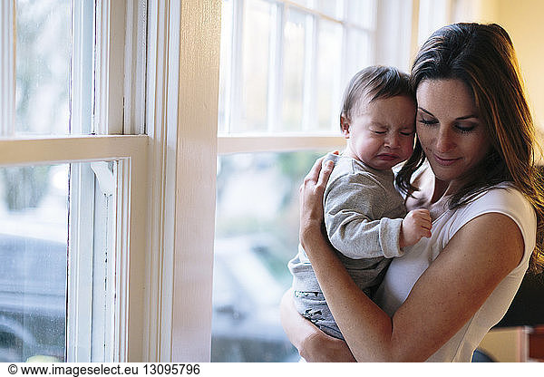 Mother with baby standing by window at home