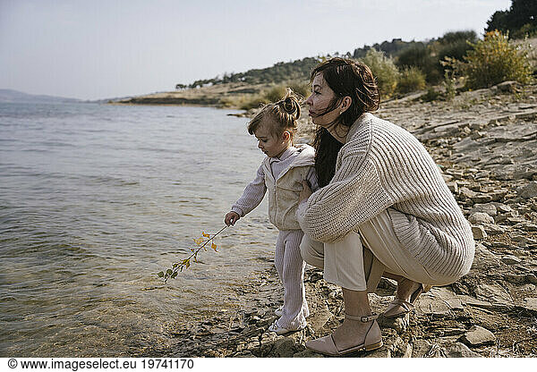 Mother with daughter holding twig near lake