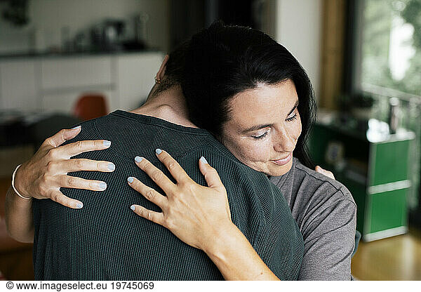 Mother with eyes closed embracing son at home