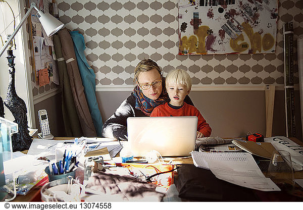Mother with son using laptop on messy table at home