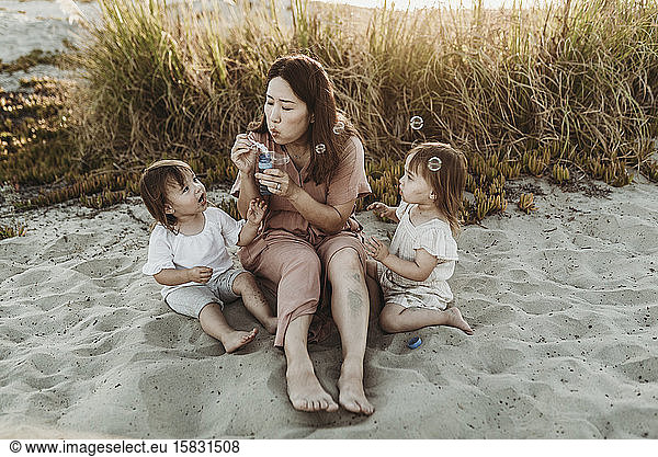 Mother with young twin daughters blowing bubbles at the beach