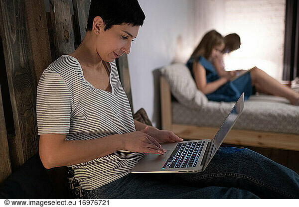 Mother working on laptop near daughters in evening