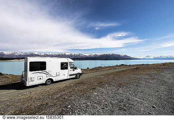 Motorhome in dirt road with blue lake and snow caped mountains