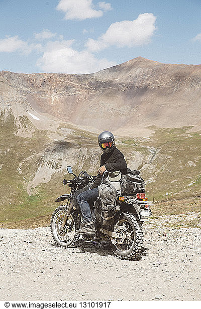 Motorradfahrer mit Motorrad  der am sonnigen Tag auf dem Berg gegen den Himmel sitzt