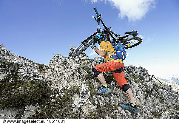 Mountain biker carries his bike on shoulder and walking uphill  Tirol  Austria