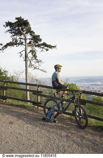 Mountain biker resting while sitting on wooden railing