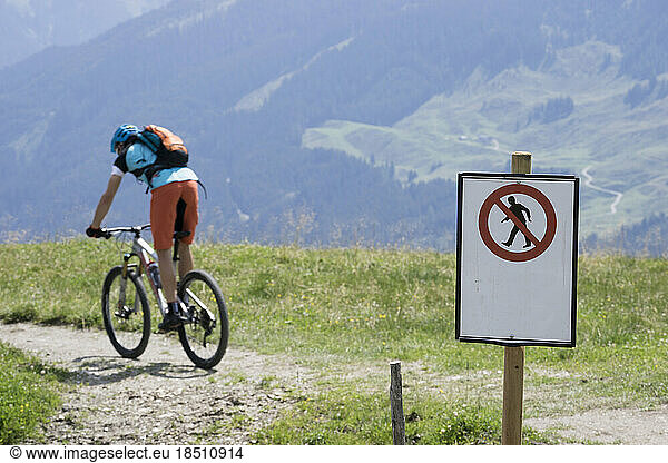Mountain biker riding on bicycle trail with warning sign  Zillertal  Tyrol  Austria